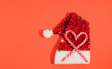 Christmas background with Heart of Christmas sweets on santas hat.  Minimal concept, red background.