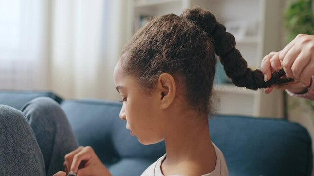 Mother doing daughter's hairstyle at home, preparing for school in the morning
