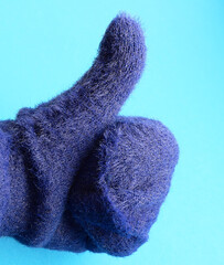 Hand in a blue mitten shows a thumbs up. Blue background. Women's clothing. Positive gestures concept.