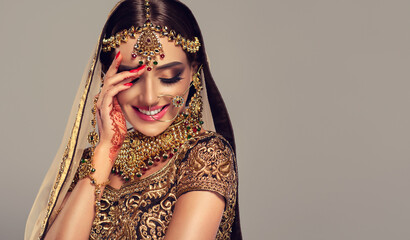 Portrait of beautiful indian girl. Young hindu woman model with golden kundan jewelry set, earrings, tikka and bracelet  . Traditional India costume lehenga choli or saree .  - obrazy, fototapety, plakaty