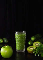 Green smoothie in a glass glass on a black background. Kiwi, apples,cucumbers and greens. Cooking healthy food.