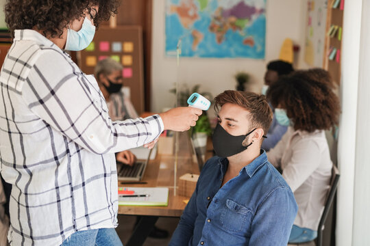 Young multiracial people working inside coworking office while measuring temparature and wearing safety mask for coronavirus outbreak