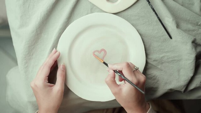 Female artist decorating ceramic plate with heart