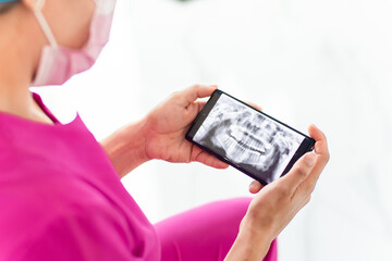 Nurse dentist in pink gown looking at an X-ray of a jaw