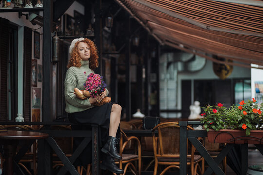 A woman in a beret and a green sweater holds a bouquet of flowers on a restaurant background