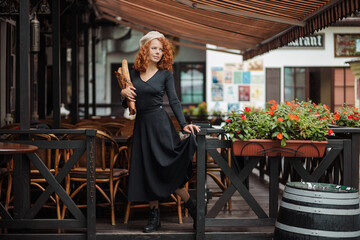 A woman in a beret and a black dress holds a baguette in her hands of the c background 