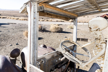 Skeleton driving an ancient broken car through the nevada desert