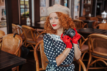 Fototapeta premium A woman in a beret and vintage dress holds a camera in her hands and takes shoots