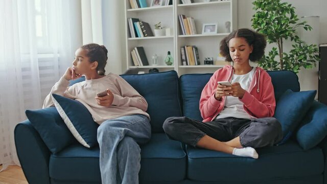 Two female teenagers feeling bored scrolling smartphone photos at home, internet