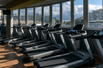 Lots of running machines near panoramic window in gym. Empty treadmills in the fitness club