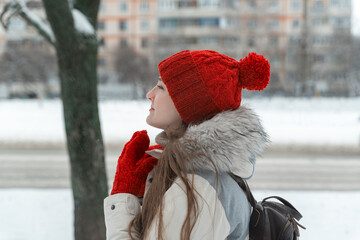 Side view portrait of frozen woman in red hat and mittens on winter city background.