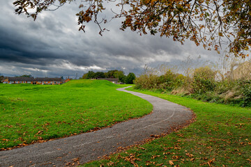 Meandering footpath located in a village park during autumn. A distant thunderstorm is developing.
