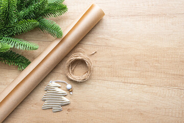 Fototapeta na wymiar Gold striped Christmas toy in the form of a Christmas tree, a roll of kraft paper and a spruce branch on a wooden background with copy space, flat lay. Eco packaging concept, zero waste. New Year.
