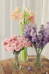 Different flowers in glass vase on wooden table. Pink roses, purple delphinium and peach amaryllis.