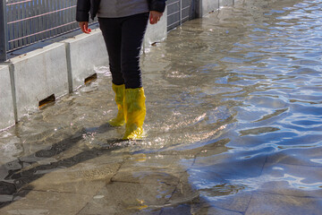 St. Marks Square during the flood. Woman with yellow boots walk in the middle of the water. High water in Venice.