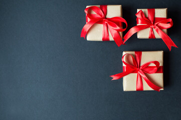 Festive concept - gifts with craft paper with a red bow on a black background. composition for christmas, new year and holidays. flat lay with place for text.
