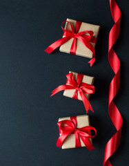 Festive concept - gifts with craft paper with a red bow on a black background. composition for christmas, new year and holidays. flat lay with place for text.
