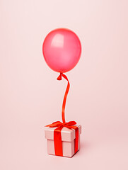 Surprise composition with color balloon and beautiful gift box with bow flying on pastel pink background. Creative birthday or Christmas concept. Minimal Valentines, anniversary or advertisement idea.
