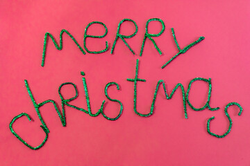 Inscription in green letters Merry Christmas on a red background, top view