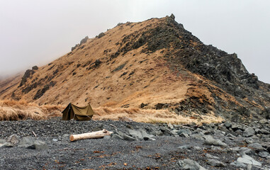 Tent made of tarpaulin under  mountain on  rocky shore.