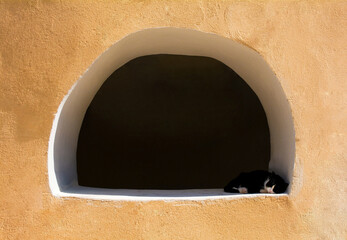 A cat sleeps in an open window in a wall in the historic coastal town of Baska on Krk island in the...