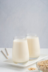 Vegetarian oat milk with creamy oatmeal taste, lactose and dairy free served in drinking glass on white wooden table for breakfast on plate with oats grain in bowl and paper straw. With copy space
