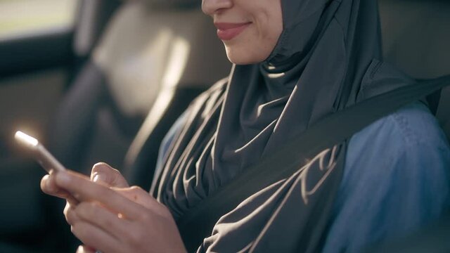 Happy middle-eastern woman doing shopping online, posting on social media in car