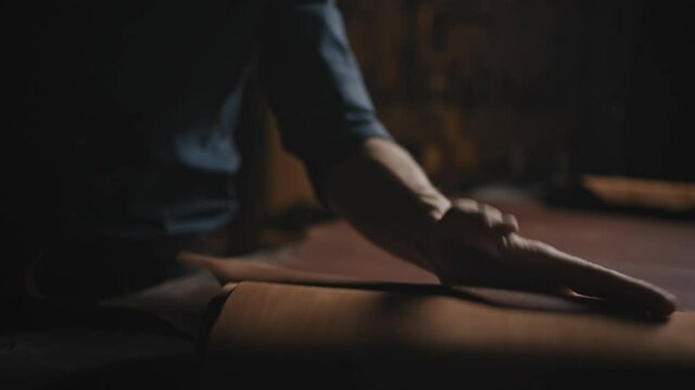 Shoes production. Unrecognizable man shoe maker rolling out piece of leather for cutting needed amount at workshop