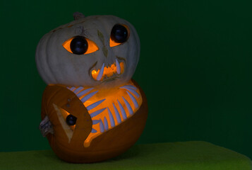 dinosaur pumpkin bites into an alien pumpkin with interior lights and green background