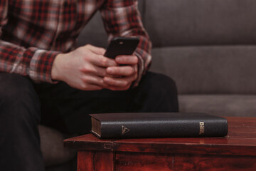 Mann sitzt am smartphone statt die Bibel zu lesen, die auf dem Tisch liegt