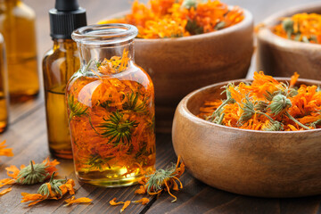 Bottles of calendula essential oil or infusion, wooden bowls and mortar of dried healthy calendula marigold flowers. Alternative herbal medicine. Aromatherapy. - obrazy, fototapety, plakaty