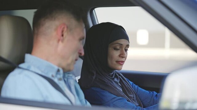 Male driving instructor giving driving lesson to woman in hijab, sitting in car