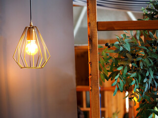 metal chandelier in loft style with a burning light bulb on a gray wall background. side view