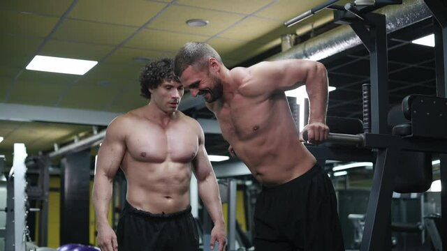 Trainer Coaches Client in Gym. Young Athletic Man doing push-ups on parallel bars.