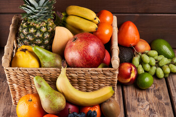 Mix of fresh juicy colorful exotic tropical fruits in basket on wooden background