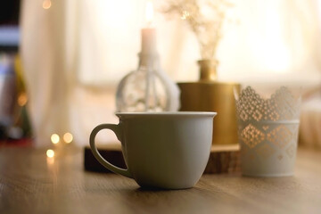 Cup of warm drink, lit candles and flowers on a table. Hygge at home. Selective focus.