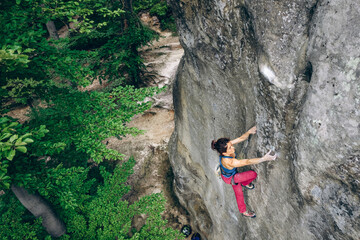 Young female rock climber climbing with rope on a rocky wall