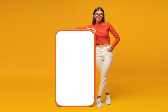 Happy young woman standing and showing blank screen of huge phone, mockup for your app