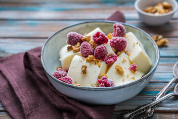 Dessert, cut into pieces of sour cream or cream jelly, garnished with walnuts and raspberries, in a gray ceramic bowl on a wooden background. Jelly recipes.