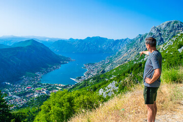 Tourist man on background on Boka Kotorska Bay and coastal towns at foot of mountain ranges. Summer blue landscape. Adriatic Sea. Montenegro.