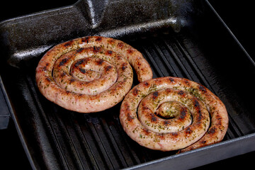 Spiral sausages on a grill pan on a dark background.