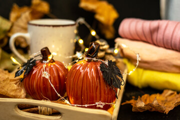 Cocoa with milk in a white mug, pumpkins, garlands, a pine cone are on a tray. Autumn yellow leaves. Knitted sweater in a pile. Autumn season. Warm home atmosphere. Cozy home.