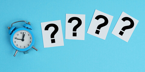 On a blue background, an alarm clock and white pieces of paper with a question sign.