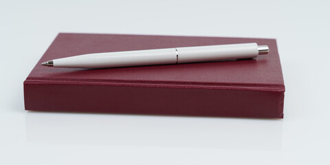 On a white background, a red notepad and a white pen.