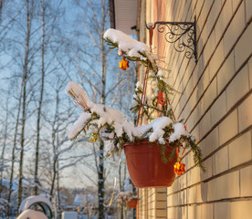 A decorative pot with a Christmas bouquet, fir branches, toys and shiny tinsel on a light brick wall.