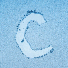 The letter C written on glass with frost in the frost in winter, close up