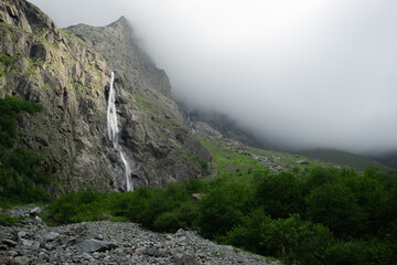 Fototapeta na wymiar Beautiful Midagrabin waterfall in sunlight in cloudy summer weather. Caucasus mountains. Russia. North Ossetia Alania