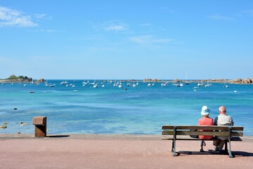 A couple of retired people sitting on a bench in front of the sea at Port-Blanc in Brittany. France