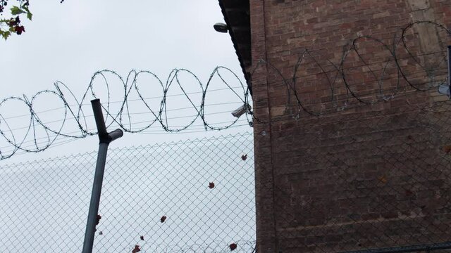 A zoom-in shot on the outdoor surveillance camera of the prison through the sharp barbed-wire fence.