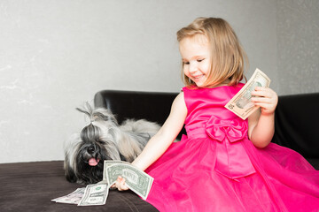 the girl is sitting on the edge of the sofa with her shih tzu dog and sharing money with her pet